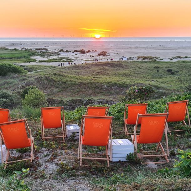 Orange Liegestühle stehen in einer Reihe und bieten einen idyllischen Blick auf den Sonnenuntergang am Strand.