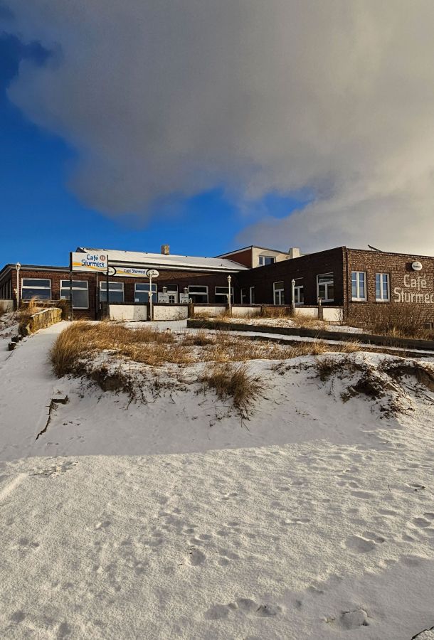 Das Café Sturmeck auf Borkum liegt idyllisch im Schnee unter einer dramatischen Wolkendecke.